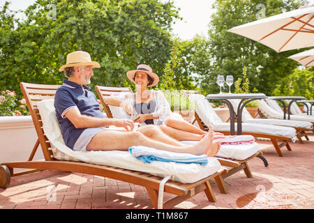 Mature couple relaxing on lounge chairs at sunny poolside Stock Photo