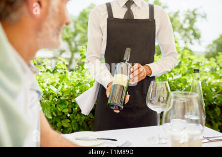 Wine steward showing wine bottle to man dining on patio Stock Photo