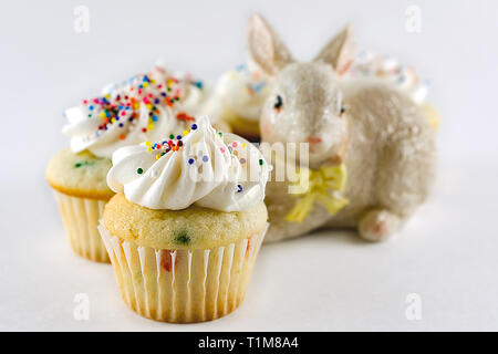 White confetti cake mini cupcake up close.  Additional cupcakes blurred in background with Easter bunny.  White background with horizontal crop. Stock Photo