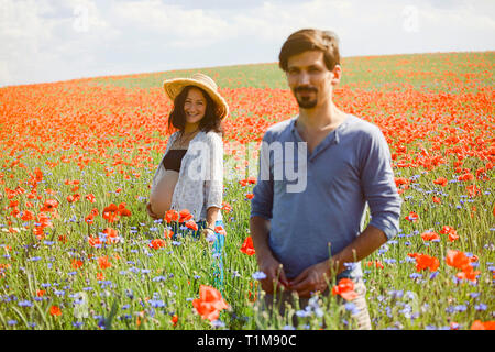 Portrait smiling pregnant couple in sunny, idyllic rural red poppy field Stock Photo