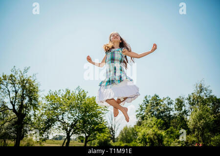 Carefree girl in dress jumping for joy in sunny backyard Stock Photo