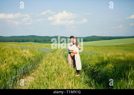 Affectionate pregnant couple hugging in sunny, idyllic rural green field Stock Photo