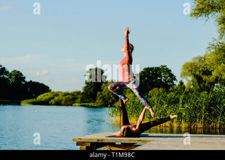 Women practicing acroyoga on sunny lakeside dock Stock Photo