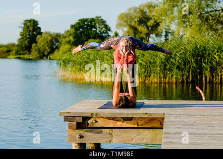 Portrait smiling women practicing acro yoga on sunny lakeside dock Stock Photo