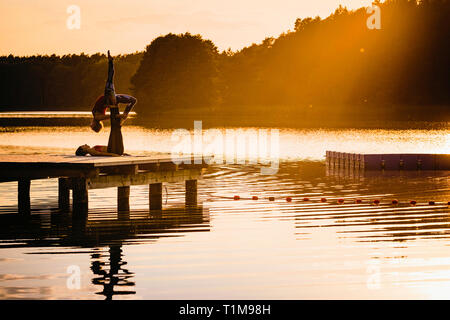 Women practicing acro yoga on lakeside dock at sunset Stock Photo