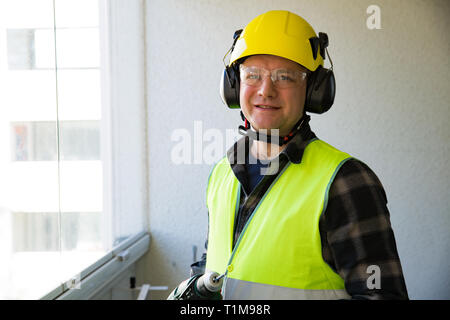 Male construction worker in hard hat with a drill and smiling at the camera. Building and renovation. Stock Photo
