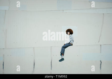 Portrait confident young man with afro sitting on sunny urban wall Stock Photo