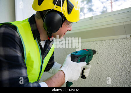 Male construction worker in hard hat drilling concrete wall with a drill. Building and renovation. Stock Photo