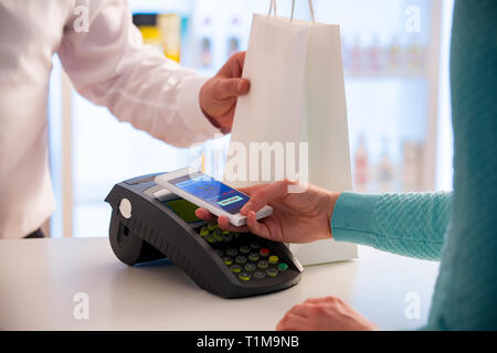 Wireless payment using smartphone and NFC technology. Close up. Customer paying with smart phone in pharmacy. Close Up shopping Stock Photo
