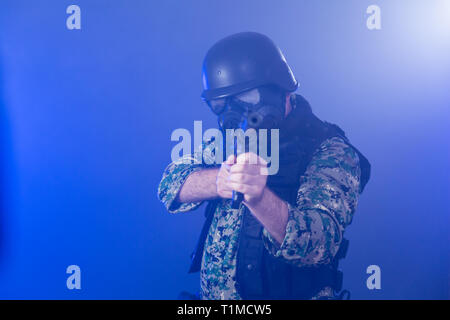 Soldier in army fatigues wearing gas mask holding assault rifle in haze of blue smoke Stock Photo