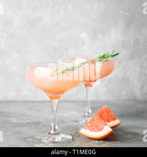 Drink grapefruit rosemary and ice in elegant glass goblets gray concrete background. Square frame Selective focus. Stock Photo