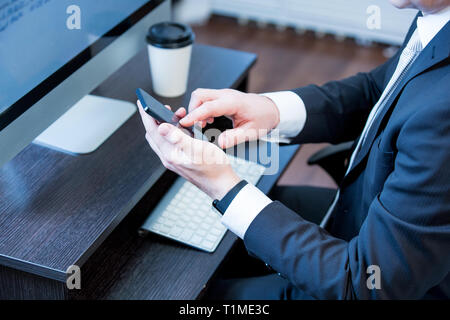 Adult man in suit working in the office. Using smart phone and computer. Hands with smart phone. man at his workplace. close-up hands Stock Photo