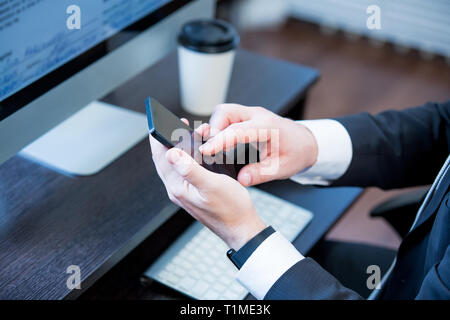 Adult man in suit working in the office. Using smart phone and computer. Hands with smart phone. man at his workplace. close-up hands Stock Photo
