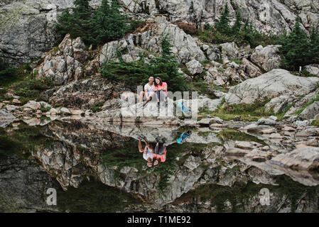 Portrait couple hiking, resting at rocky lake, Dog Mountain, BC, Canada Stock Photo