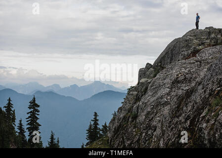 Male hiker standing on rugged mountaintop, looking at view, Dog Mountain, BC, Canada Stock Photo