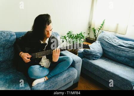 Young man practicing with his electric guitar on the sofa of his house learning. Stock Photo