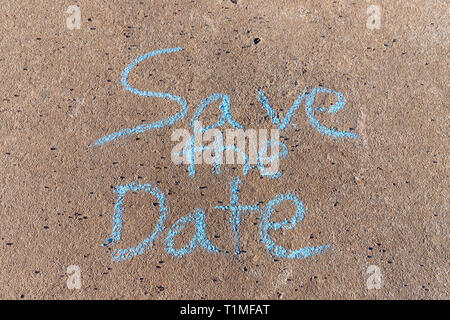 the words Save the Date written with sidewalk chalk on gray concrete pavement background Stock Photo