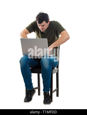 Angry young man with laptop on knees, hand on keyboard, typing a message isolated over white background. Irritated freelancer or programmer guy workin Stock Photo