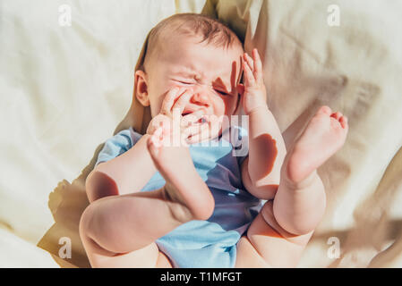 Baby lying in the sun angry and crying calling his parents. Stock Photo
