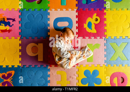 Adorable smiling baby seen from above in pajamas, lying on his back in his toy room. Stock Photo