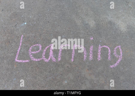 the word Learning written with pink sidewalk chalk on gray concrete pavement background Stock Photo