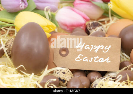 Happy Easter Easter Celebration written on a label with chocolate eggs and pastel colored tulips Stock Photo