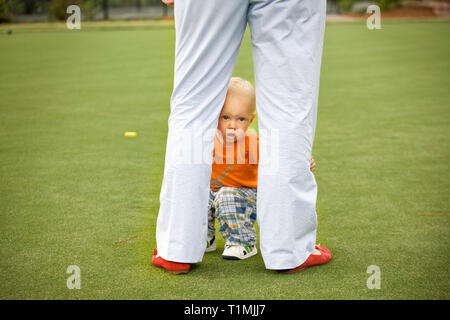 A male toddler hides behind his father's legs on a croquet field Stock Photo