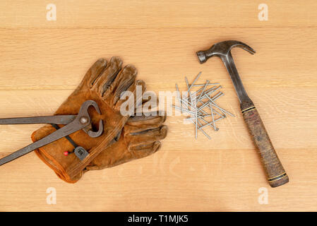 Vintage Pair Of Long Handle Cutting Pliers Nippers and well Worn Leather Work Gloves Old Hammer and Nails Wood Background Stock Photo