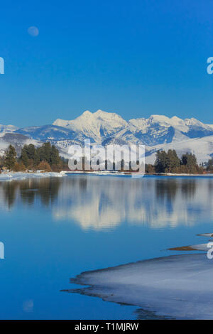 moon rising over the flathead river and mission mountains in winter near dixon, montana Stock Photo