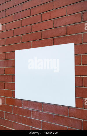 Abstract photograph of a Blank white rectangular sign panel fastened to a plain red brick wall Stock Photo