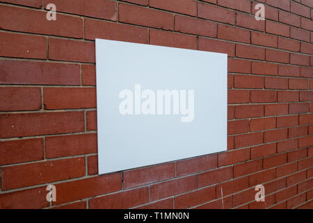Abstract photograph of a Blank white rectangular sign panel fastened to a plain red brick wall Stock Photo