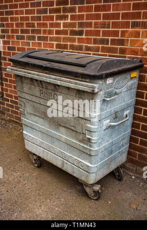 Industrial 660 Litre Metal Wheelie Bin against a plain red brick wall outside commercial premises Stock Photo