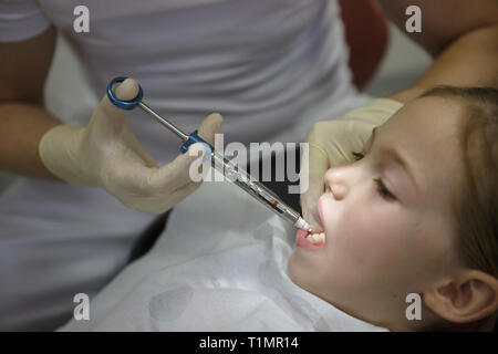 Scared little girl at dentist office, getting local anesthesia injection into gums, dentist numbing gums for dental work. Pediatric dental care concep Stock Photo