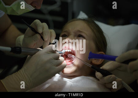 Scared little girl at the dentists office, in pain during a treatment. Pediatric dental care and fear of dentist concept. Stock Photo