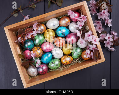 Colorful quail Easter eggs in a wooden box, on a bed of hay, with flowering branches of purple leaf plum tree Stock Photo