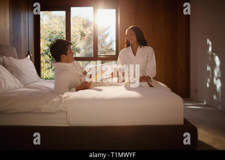 Couple in bathrobes relaxing on hotel bed Stock Photo