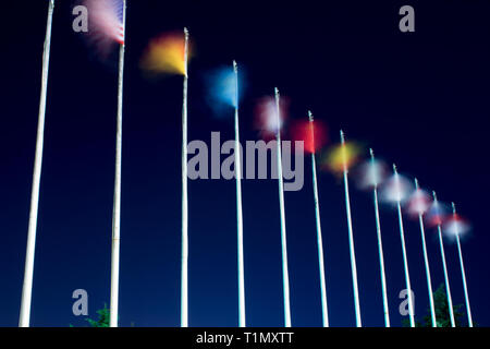 Long exposure flags. Waving flags on the wind at night. Different countries flags are on the pillars Stock Photo