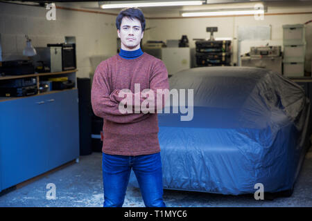 Portrait confident man standing in front of covered car in garage Stock Photo