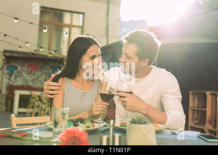 Cute happy couple cuddling together while clinking glasses with red wine Stock Photo