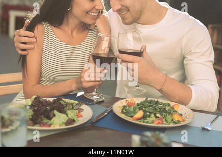 Strong handsome man hugging his skinny lady and clinking glasses with wine Stock Photo