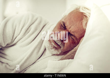 Close-up portrait of an elderly bearded wrinkled man experiencing pain Stock Photo