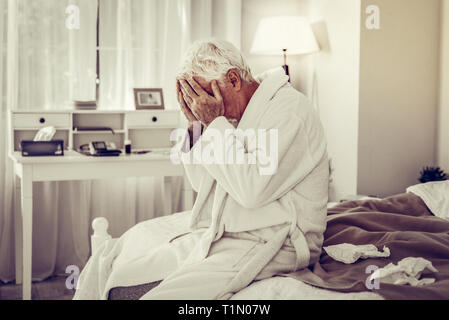 Sick man closing face with hands and sitting on bed Stock Photo