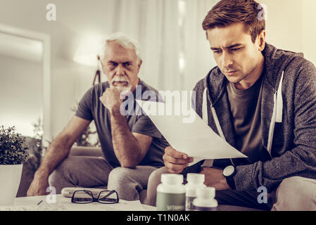 Focused son reading the assessment of doctor of his father Stock Photo