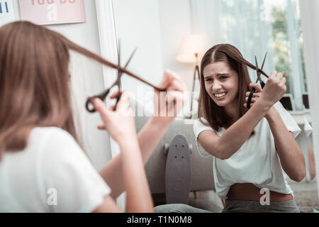 Stressed woman trying to cut her hair Stock Photo