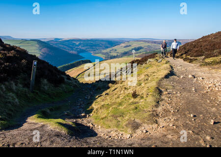 Two ramblers on the footpath near Whinstone Lee Tor, Derwent Edge, English Peak District, with Ladybower Reservoir in the distance Stock Photo