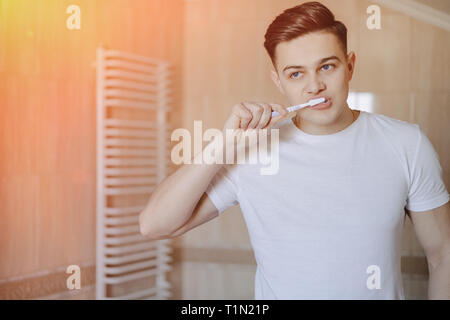 morning hygiene, the boy brushes his teeth near the mirror in the bright bathroom Stock Photo