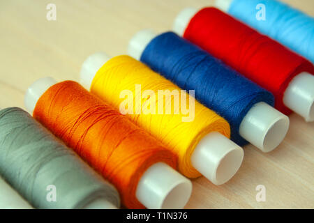 Many multi colored yarn strings bobbins on bright wooden background. Texture of colored thread. Concept of sewing, hobby image. Stock Photo