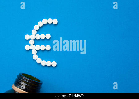 white pills in the shape of a euro are scattered on a blue background next to a dark bottle. Stock Photo