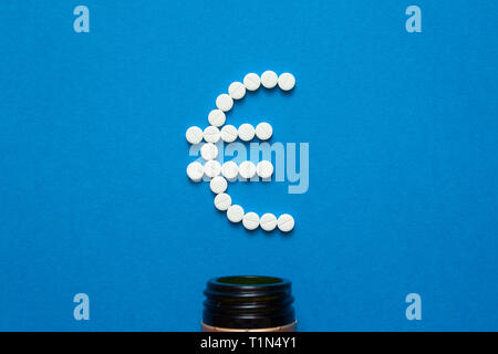 white pills in the shape of a euro are scattered on a blue background next to a dark bottle. Stock Photo