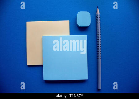 Two blue and yellow square stiker blocks arranged with the silver pencil and the blue eraser on the dark blue background. Stock Photo